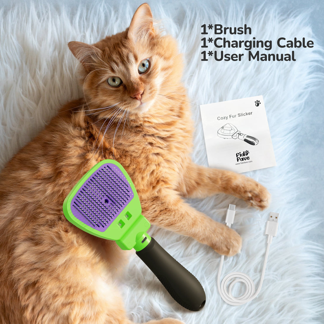An orange tabby cat lying on white fleece beside the green-and-purple self-cleaning cat slicker brush, a USB-C charging cable and a folded user manual; printed text reads “1*Brush 1*Charging Cable 1*User Manual”